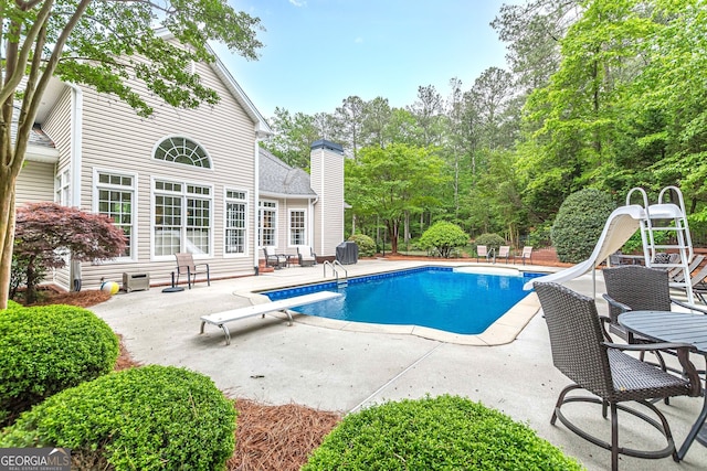 outdoor pool featuring a diving board, a water slide, and a patio area