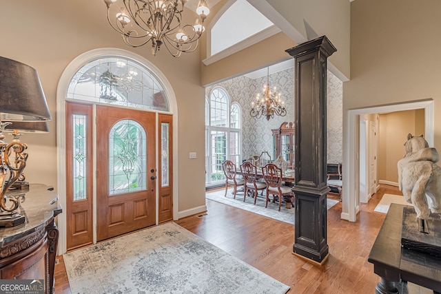 foyer with a towering ceiling, an inviting chandelier, a wealth of natural light, and light wood-type flooring