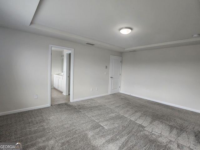 carpeted empty room featuring visible vents, a tray ceiling, and baseboards