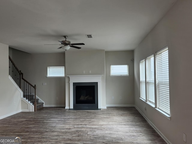 unfurnished living room featuring a fireplace with flush hearth, stairway, a ceiling fan, visible vents, and wood finished floors