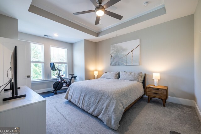 carpeted bedroom with ceiling fan, visible vents, a raised ceiling, baseboards, and ornamental molding