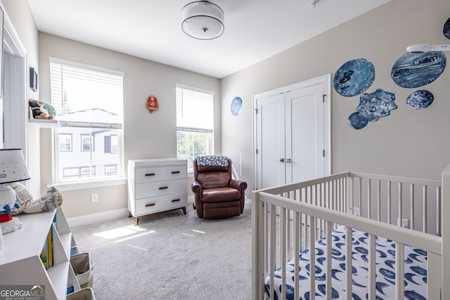 bedroom with a closet, a crib, baseboards, and carpet flooring