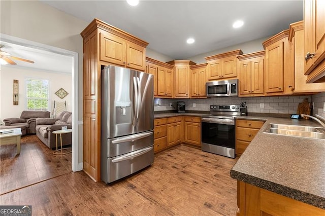 kitchen featuring a sink, appliances with stainless steel finishes, dark countertops, wood finished floors, and backsplash
