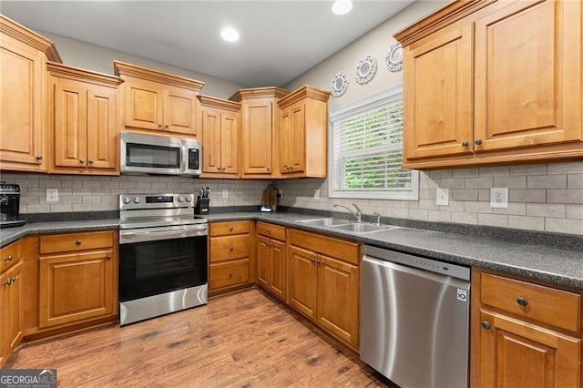 kitchen featuring dark countertops, a sink, stainless steel appliances, and light wood-type flooring