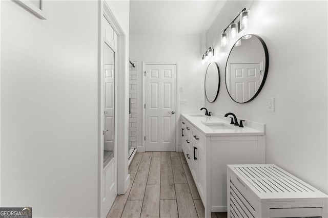 full bathroom featuring double vanity, wood finished floors, a shower, and a sink
