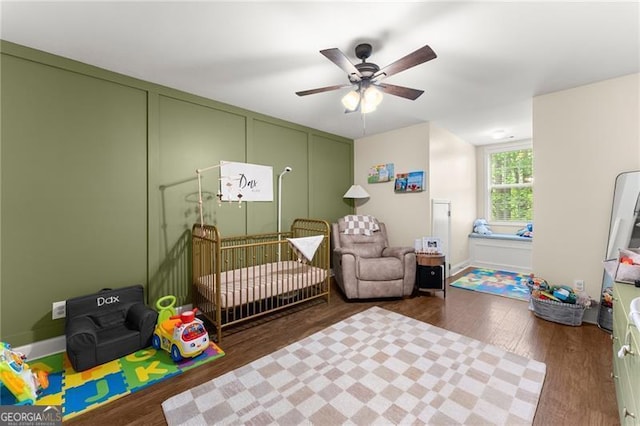 bedroom featuring wood finished floors, ceiling fan, and a crib