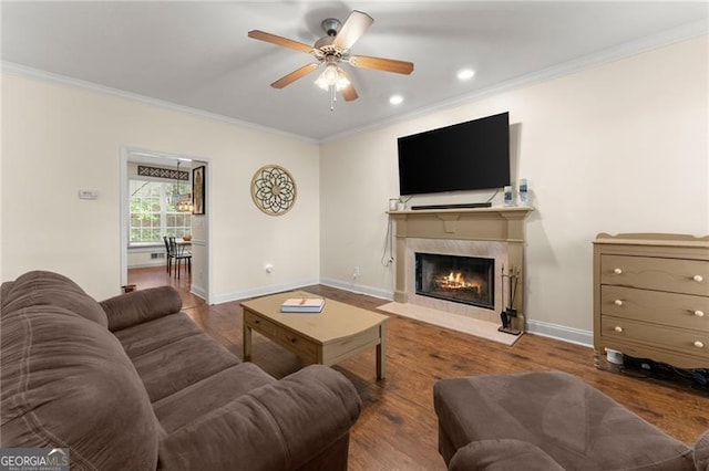 living area featuring a fireplace with flush hearth, crown molding, baseboards, wood finished floors, and a ceiling fan