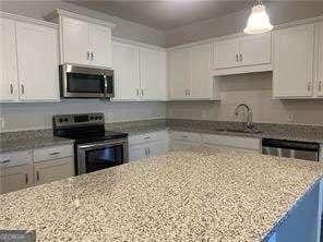 kitchen featuring light stone counters, white cabinets, a sink, stainless steel appliances, and hanging light fixtures