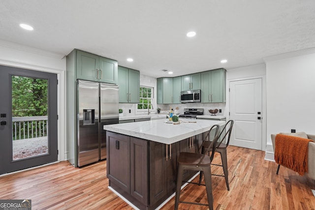 kitchen featuring light wood-style flooring, stainless steel appliances, green cabinets, ornamental molding, and backsplash