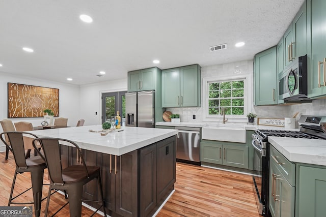 kitchen featuring green cabinetry, light wood-style floors, appliances with stainless steel finishes, a sink, and visible vents