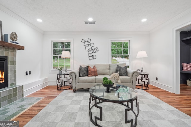 living area featuring a tiled fireplace, visible vents, wood finished floors, and baseboards