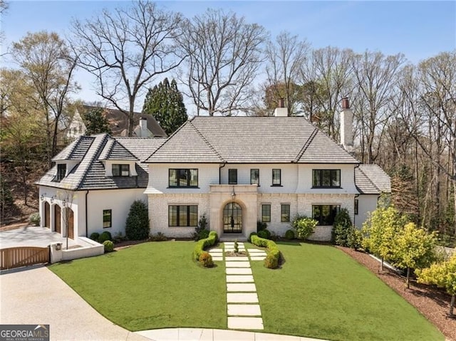 french country style house with brick siding, a front yard, a chimney, and concrete driveway