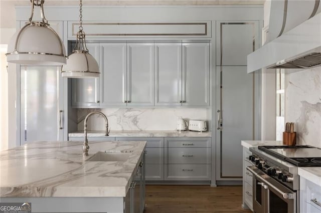kitchen with exhaust hood, light stone countertops, a sink, range with two ovens, and pendant lighting