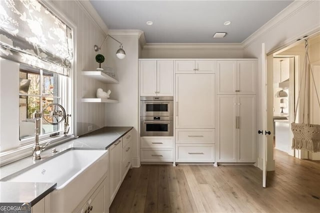 kitchen with crown molding, open shelves, double oven, light wood-type flooring, and a sink