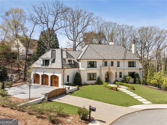 french country style house with concrete driveway, a chimney, and a front lawn