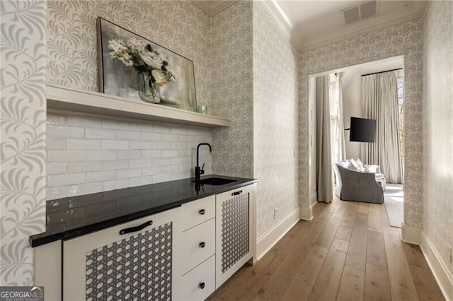 bar featuring wallpapered walls, ornamental molding, a sink, and hardwood / wood-style floors