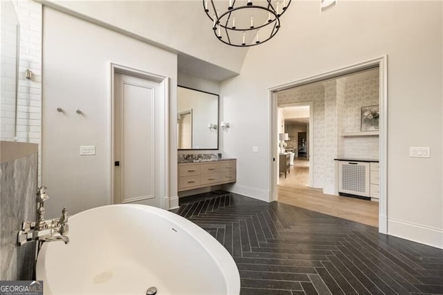 full bath with vanity, baseboards, a soaking tub, and a chandelier