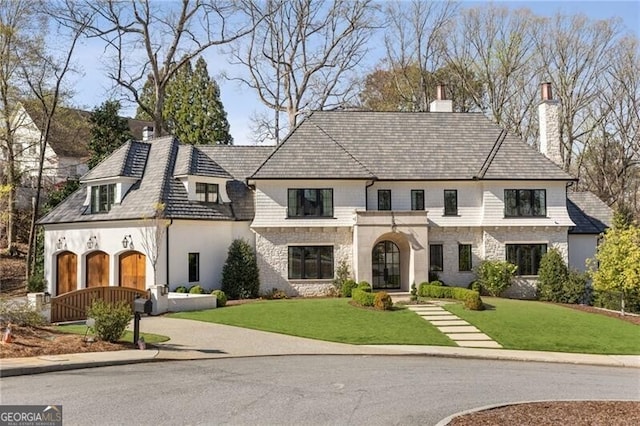 french country home featuring a front yard, driveway, a chimney, and stone siding