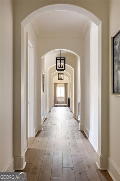 hall featuring arched walkways, ornamental molding, baseboards, and hardwood / wood-style floors