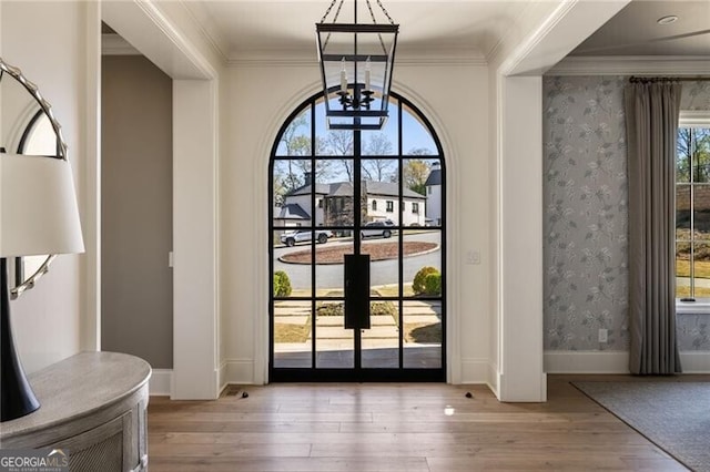 doorway to outside featuring ornamental molding, a chandelier, hardwood / wood-style flooring, and wallpapered walls