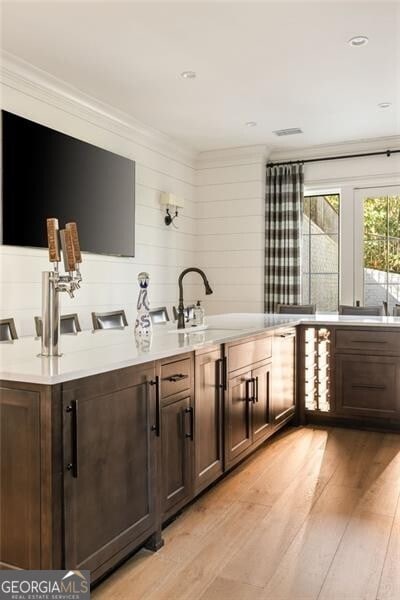 bar with crown molding, a sink, light wood-style flooring, and visible vents