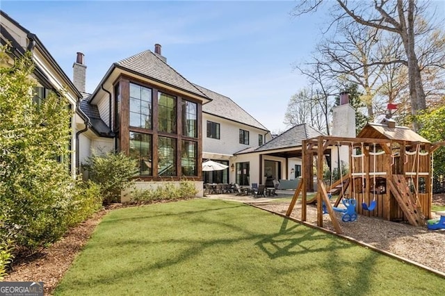 rear view of property featuring a lawn, a patio, a chimney, and a playground