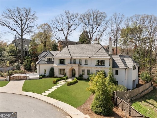 view of front facade with a chimney, a front yard, a gate, fence, and stucco siding