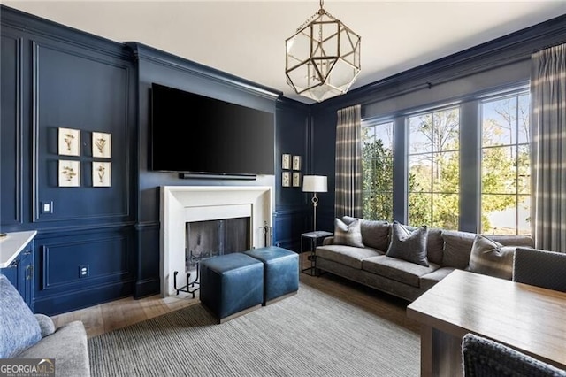 living area featuring crown molding, an inviting chandelier, a decorative wall, wood finished floors, and a fireplace
