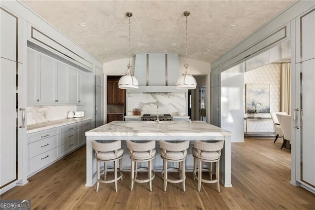 kitchen with light stone countertops, a breakfast bar, hardwood / wood-style floors, lofted ceiling, and custom exhaust hood