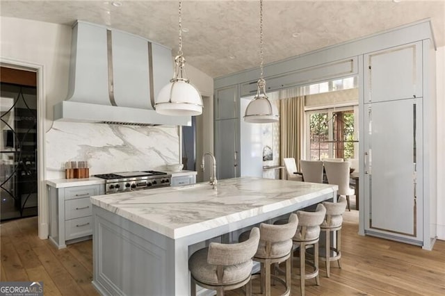 kitchen with light wood-style floors, decorative backsplash, a center island with sink, and a sink
