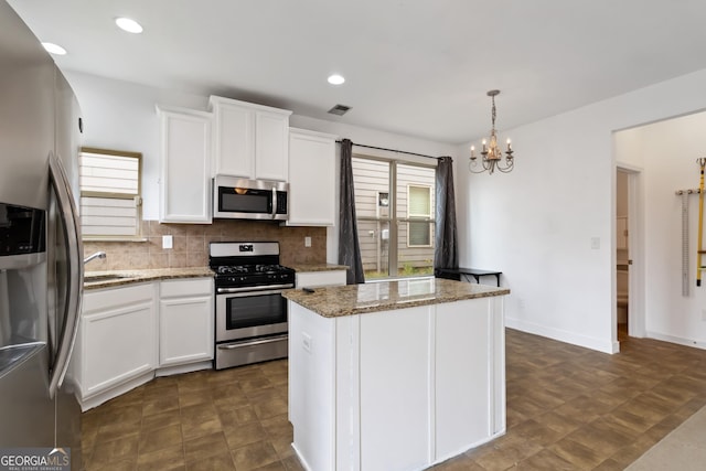 kitchen with stainless steel appliances, backsplash, light stone counters, a center island, and a chandelier