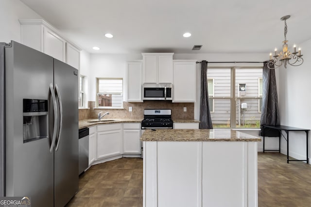 kitchen with appliances with stainless steel finishes, a sink, white cabinetry, backsplash, and a chandelier
