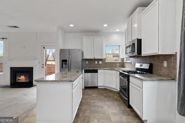 kitchen with appliances with stainless steel finishes, a kitchen island, a sink, white cabinets, and light stone counters