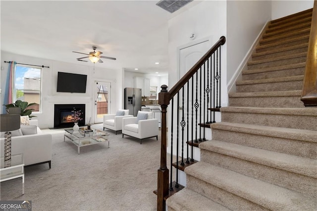 carpeted living room with stairway, ceiling fan, healthy amount of natural light, a warm lit fireplace, and recessed lighting