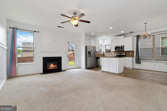 unfurnished living room with a chandelier, a ceiling fan, light carpet, baseboards, and a fireplace with flush hearth