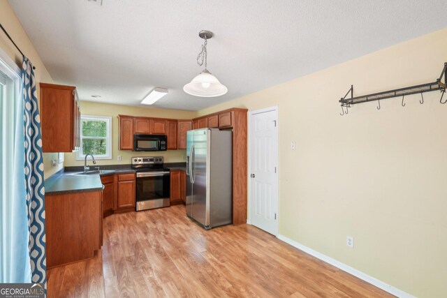 140 Spring Cir, Senoia, GA 30276 - kitchen with brown cabinets, stainless steel appliances, decorative light fixtures, light wood-style flooring, and dark countertops