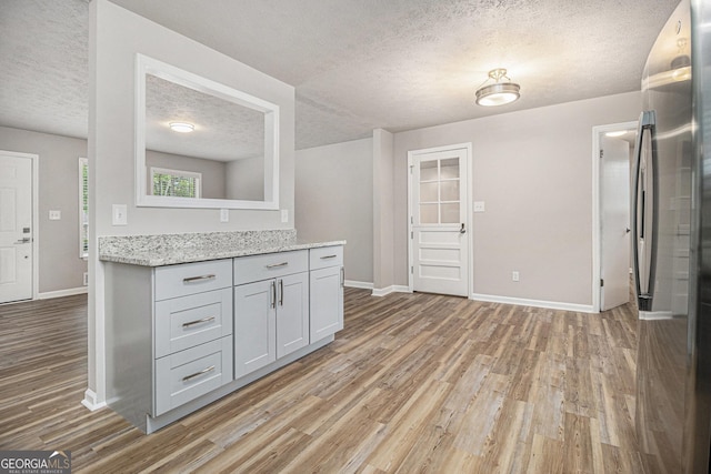 898 Doeskin Dr NW, Conyers, GA 30012 - kitchen with a textured ceiling, light wood-style floors, baseboards, light stone countertops, and freestanding refrigerator