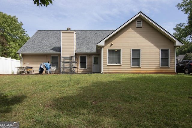 rear view of property with a chimney, fence, a yard, and roof with shingles