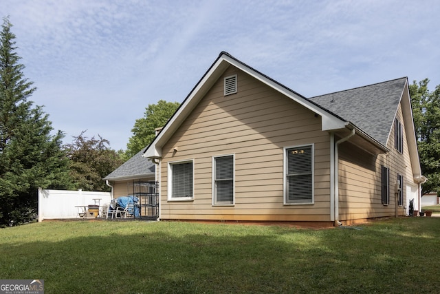 rear view of property with a lawn, roof with shingles, and fence