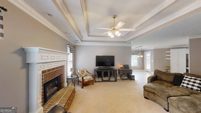 living area featuring light colored carpet, ornamental molding, a brick fireplace, a ceiling fan, and a tray ceiling