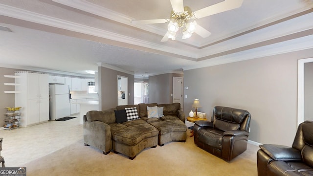 living room with a raised ceiling, ornamental molding, ceiling fan, and light colored carpet