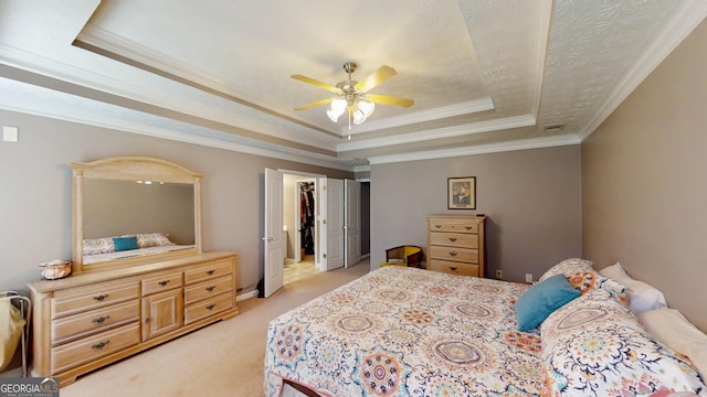 bedroom featuring a closet, ceiling fan, a tray ceiling, ornamental molding, and light colored carpet