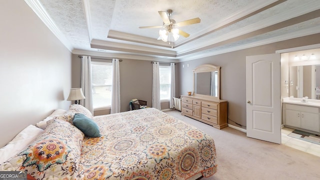 bedroom with crown molding, ceiling fan, a tray ceiling, light carpet, and ensuite bath