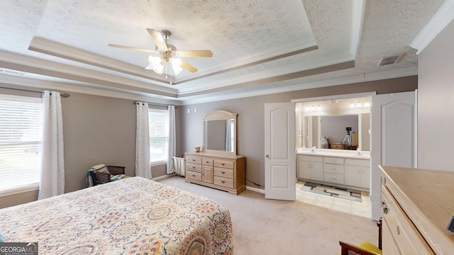 bedroom featuring a textured ceiling, light colored carpet, a tray ceiling, ornamental molding, and ensuite bath