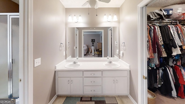 full bath with double vanity, a spacious closet, a ceiling fan, and a sink