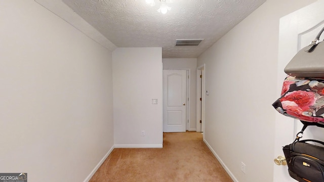 hallway with baseboards, visible vents, light carpet, and a textured ceiling