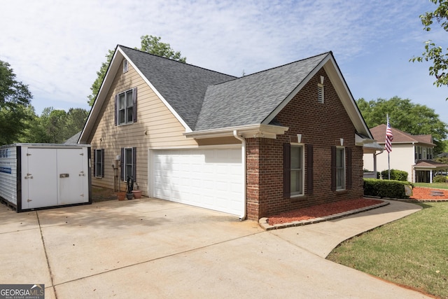 view of side of home featuring concrete driveway, a storage unit, roof with shingles, brick siding, and a garage