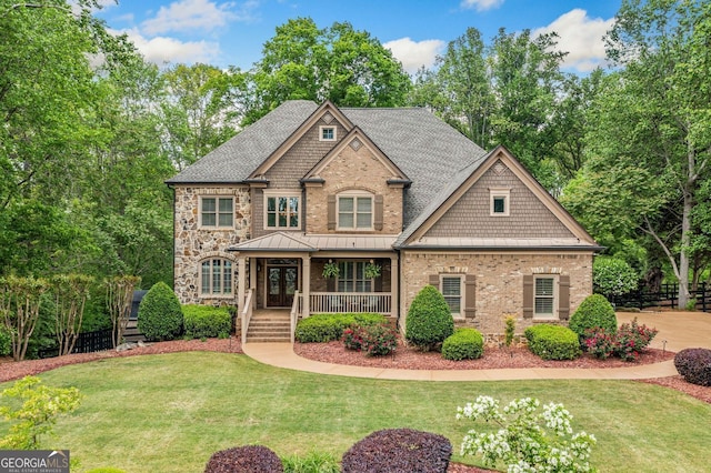 view of front of home with a front lawn, covered porch, stone siding, roof with shingles, and brick siding