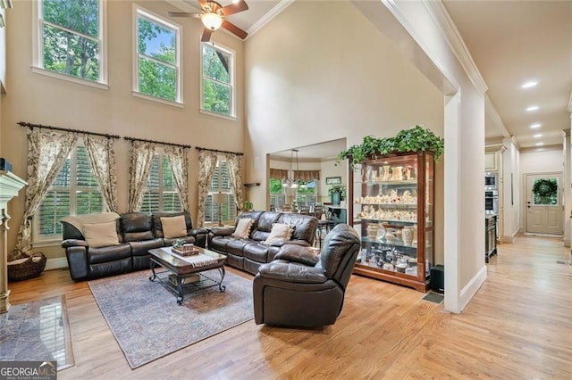 living area with ceiling fan, light wood-style flooring, baseboards, a towering ceiling, and ornamental molding