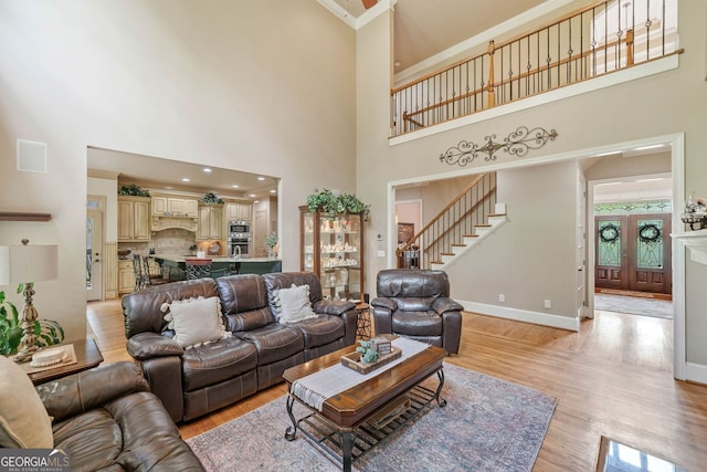 living area featuring stairway, baseboards, a high ceiling, and light wood-type flooring